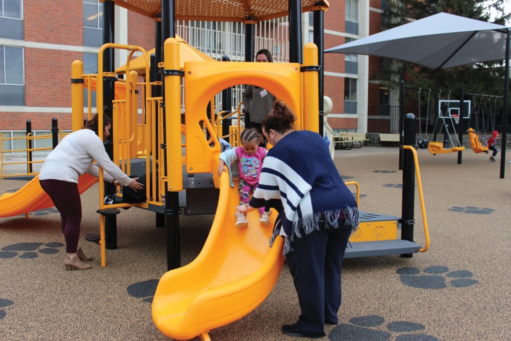A woman helps a kid slide down a slide on the SHP Inclusive Playground set