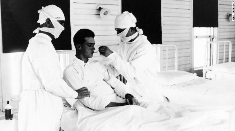 Black and white photo of male patient attended by 2 medical providers wearing face coverings