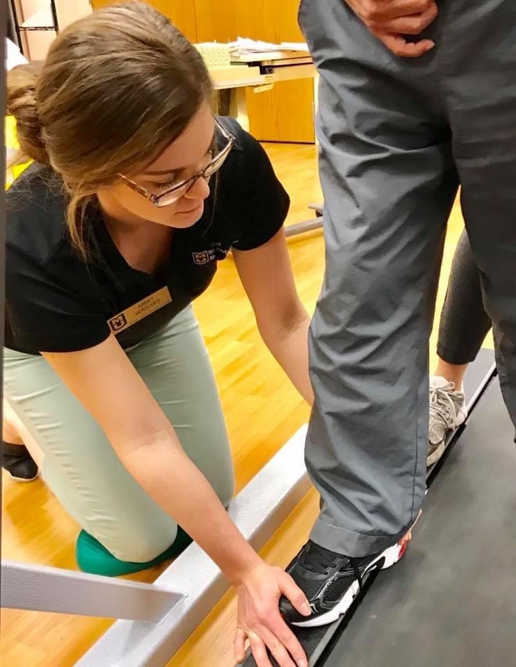 Abbey Twehous kneels next to a client's foot on a treadmill in the PhysZOU clinic 