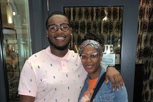 A tall Black man stands with his arm around the shoulder of a Black woman