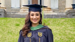 Woman with long brown hair wearing a graduation cap and gown