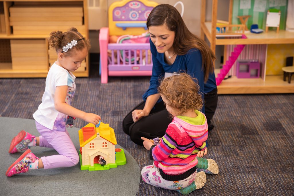 Student sits on the floor with preschoolers while administering therapy