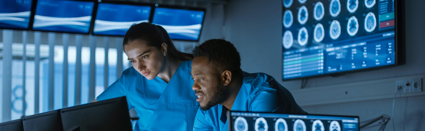 two health care workers in blue scrubs look at computer screen with brain images