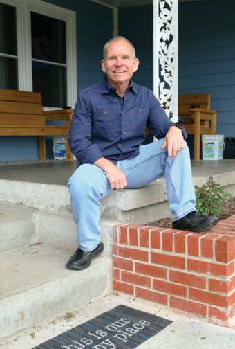 A man sits on the corner of a patio in front of a blue house