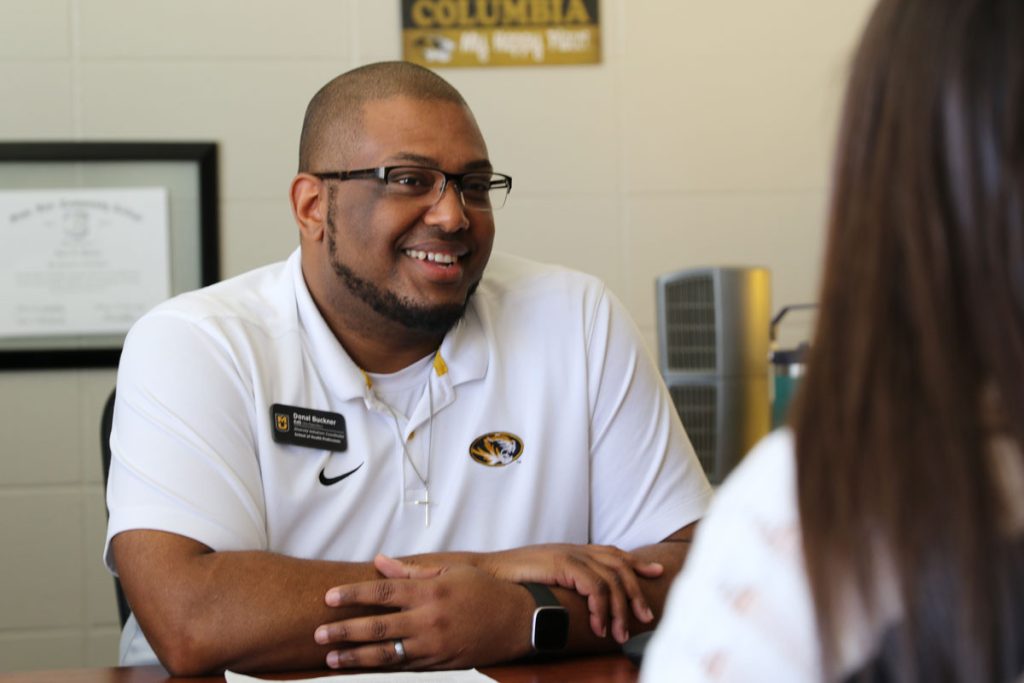 Donal Buckner at his desk listening to a student