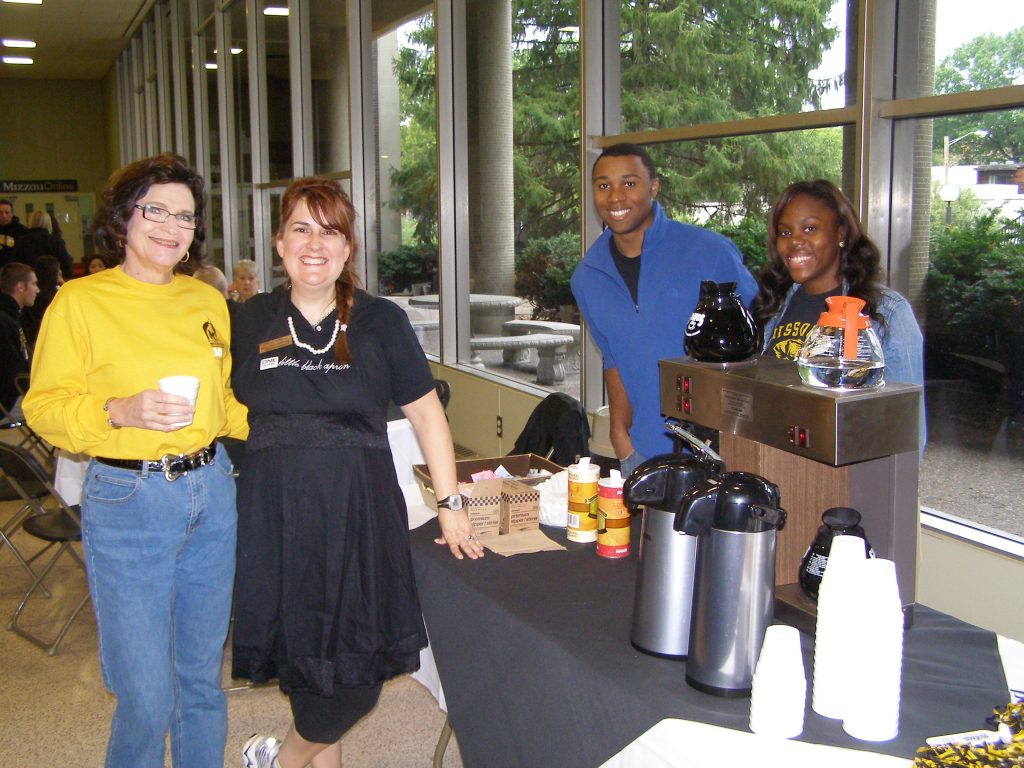 Nancy Fay stands with colleagues near a coffee station.