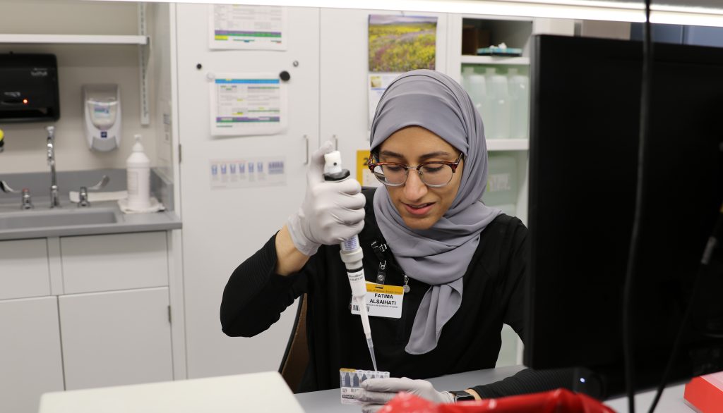 A woman wearing a hijab uses a pipette in a lab.