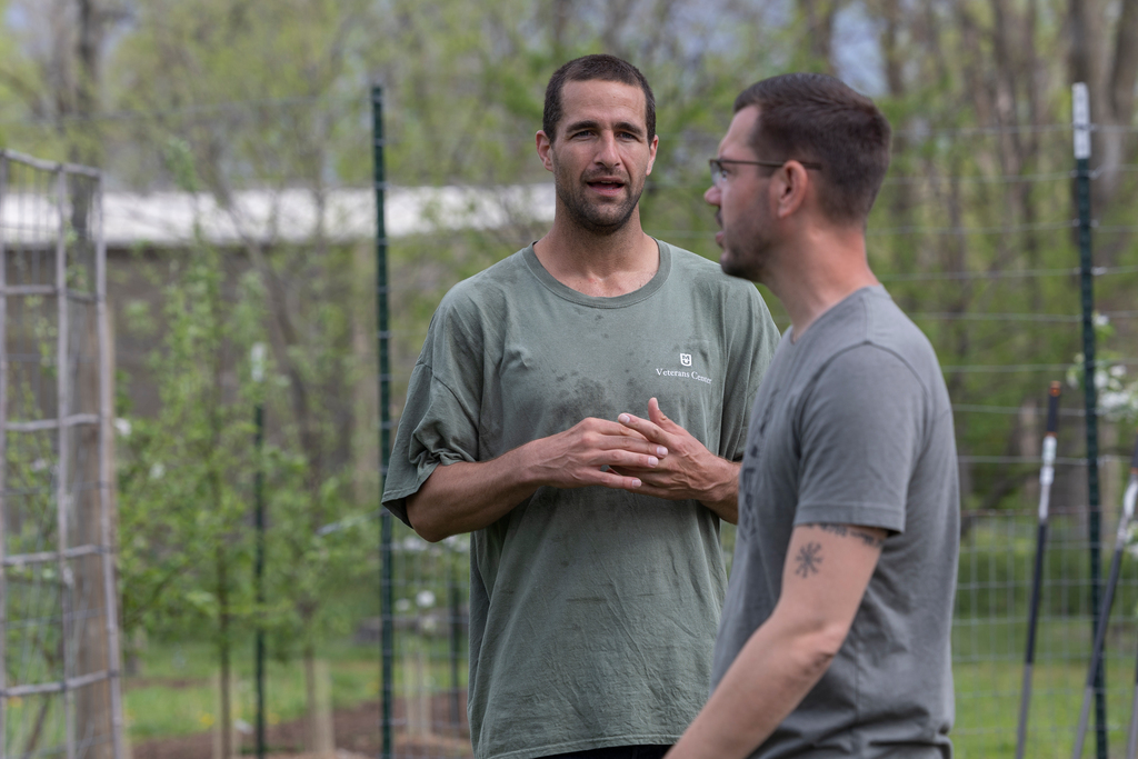 Two men talk among crops in a farm.