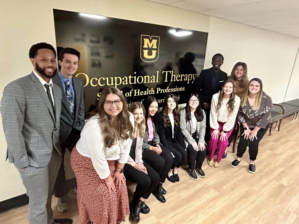 A group of students pose for a photo in front of a Mizzou Department of Occupational Therapy sign.