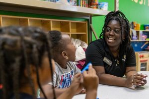 A woman smiles while speaking with two young children at a preschool.