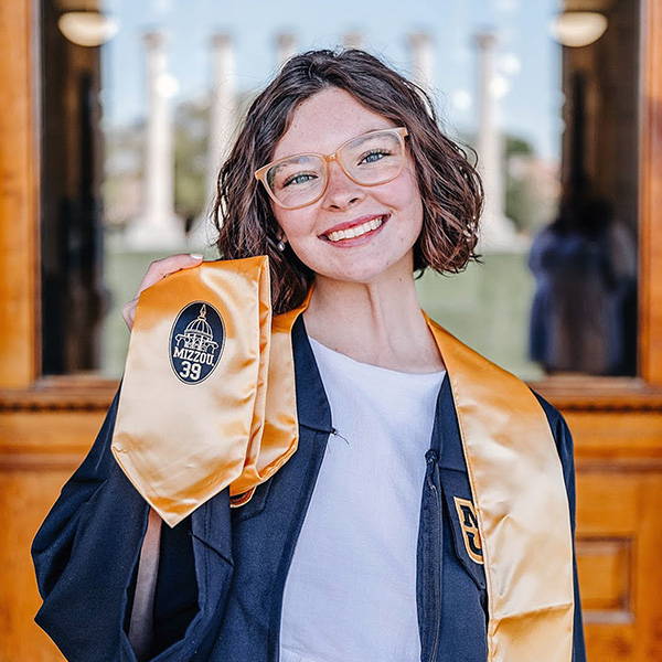 A young woman holds up a graduation sash