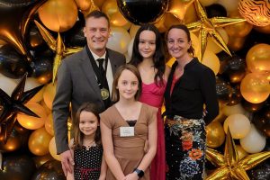 A family stands in front of yellow and gold balloons