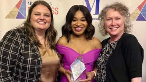 Two women stand together with Christine Woods, who is holding an award for progress in health care