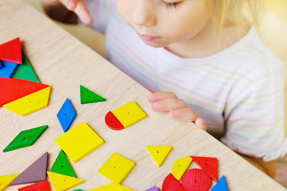 A young child looks at a table of colorful wooden shapes