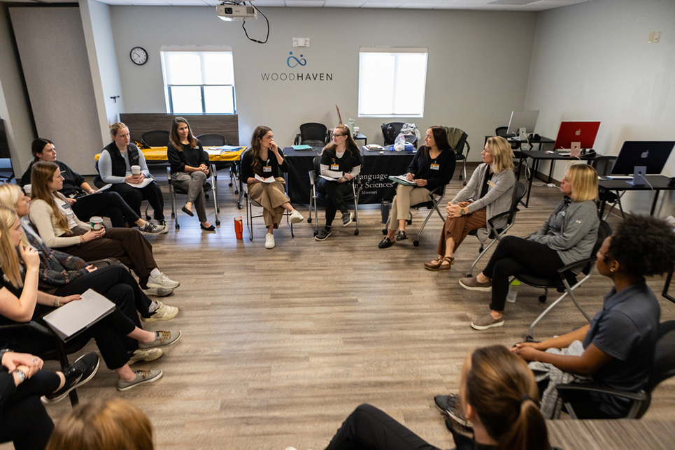 A group of students and faculty members sit in a circle to compare notes