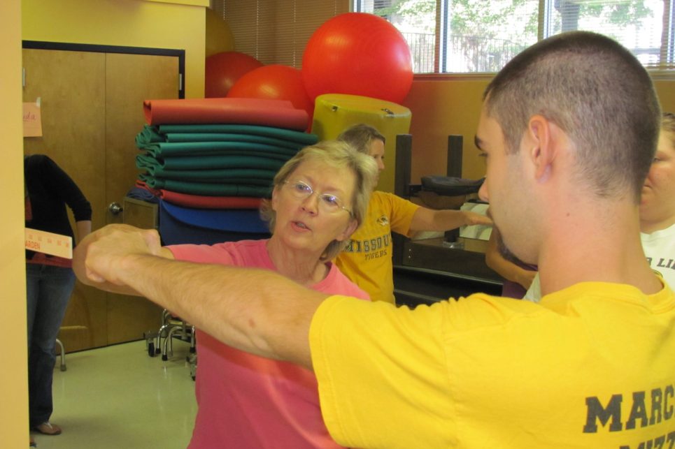 A woman shows a young man how to measure functional reach