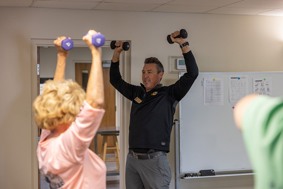 A man leads a class through a weightlifting exercise