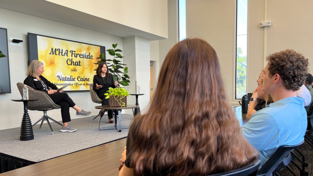 two women have a conversation on stage while the audience watches