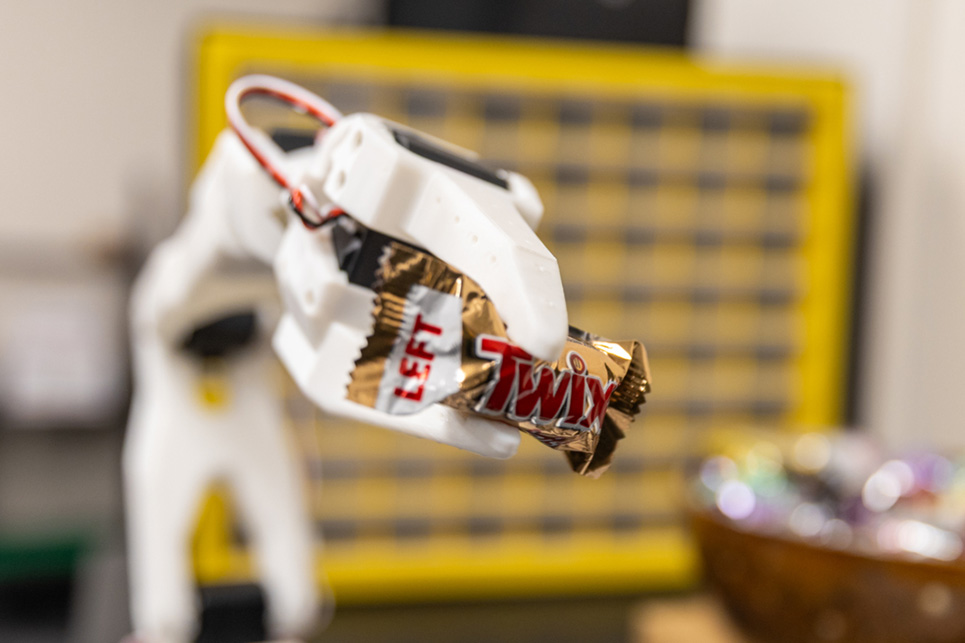 A robotic arm holds a Twix candy bar