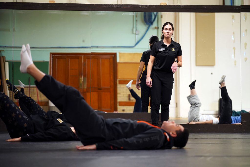 A man stretches in the foreground while a woman observes