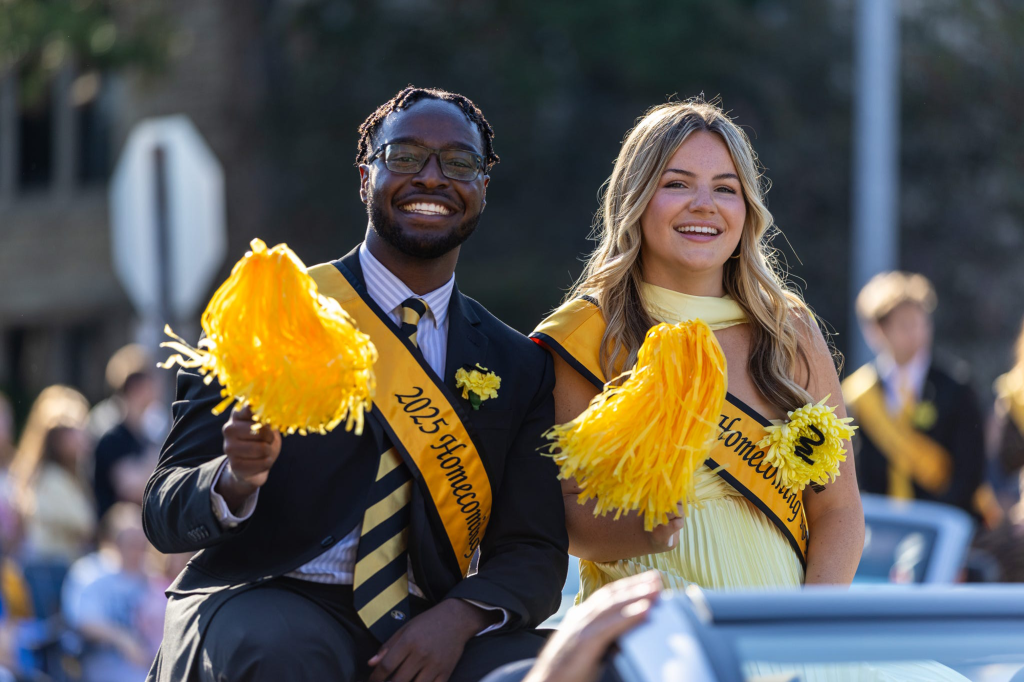 A young man and woman sit on a car in a parade