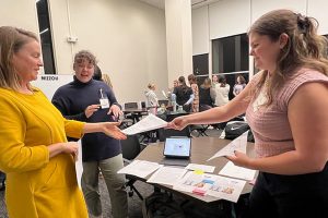 A woman hands a packet of paper to another woman