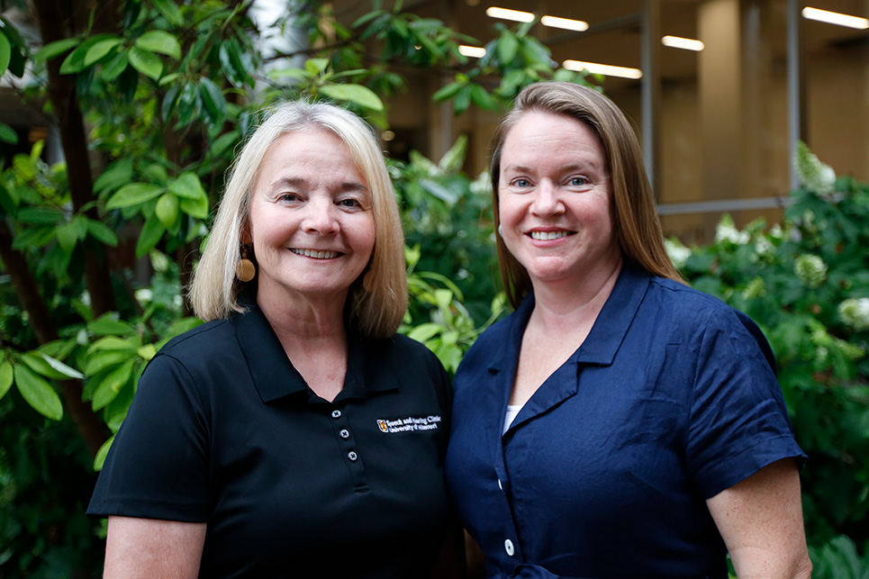 Two women stand in front of greenery